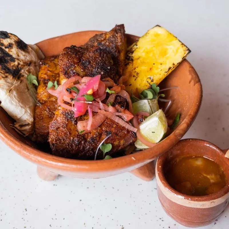 Al pastor ribs in a clay cazuela with grilled pineapple and pickled onion