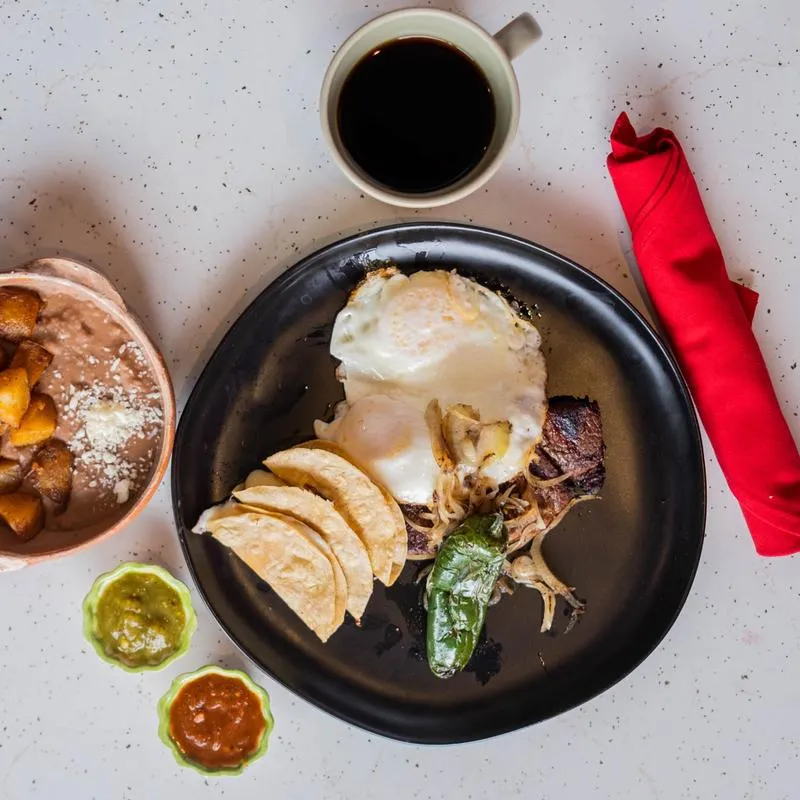 A brunch plate from above: two eggs, tortillas, chile toreado, refried beans with breakfast potatoes, salsas and coffee