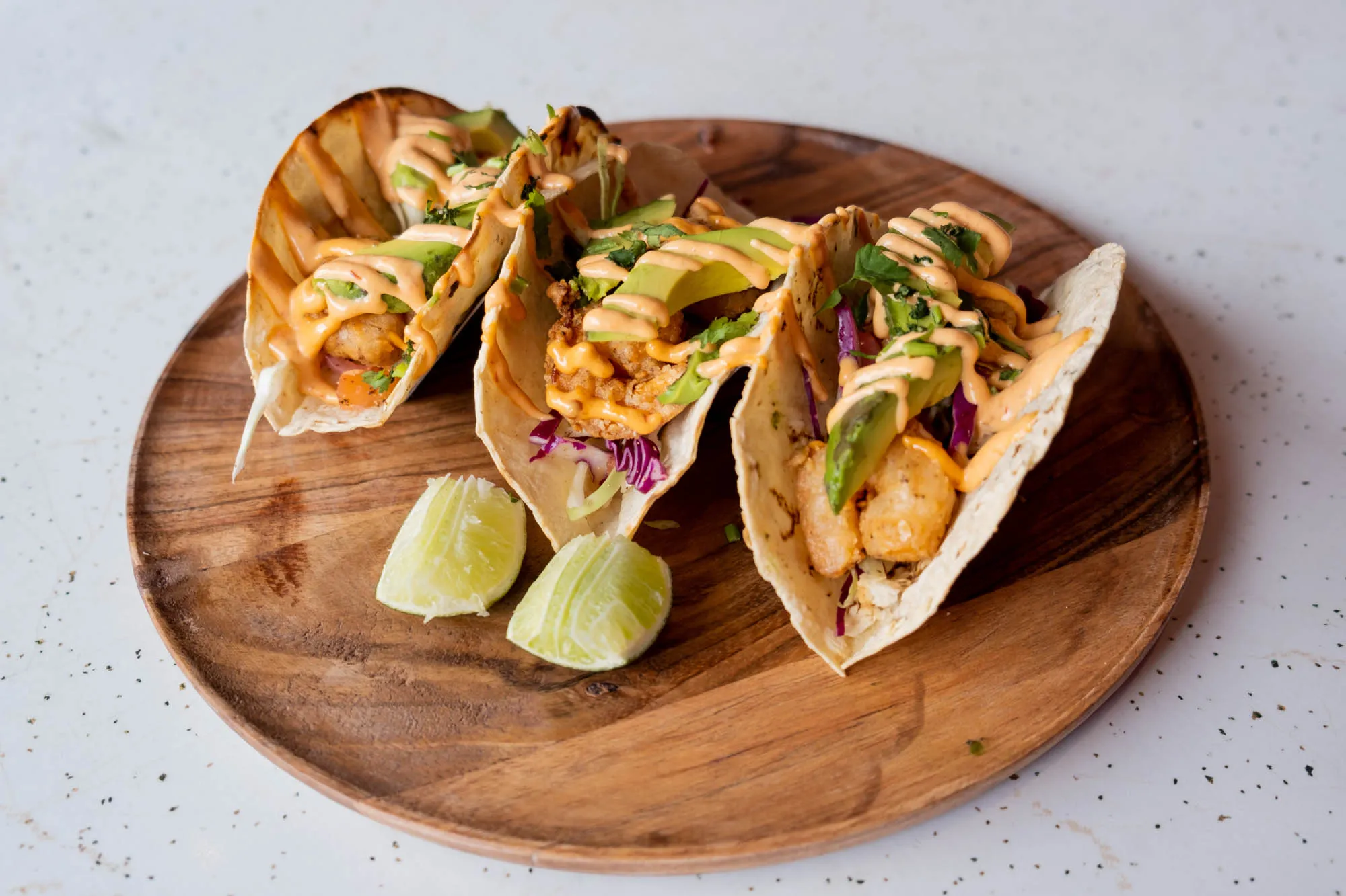 Three tacos with slaw and lime on a round wooden board