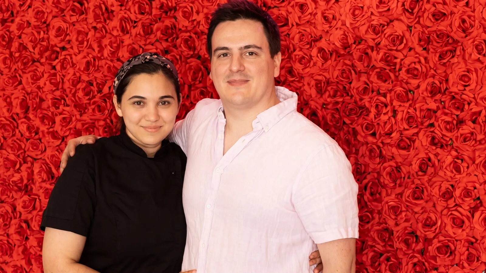 Gaby Hinojosa and Charlie Gonzalez, the chefs and owners of Panfila, together against a wall of red roses