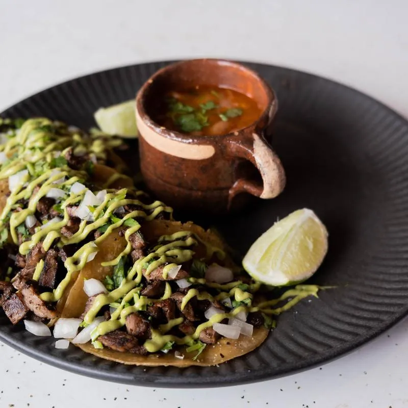 Tacos with onion and avocado salsa alongside a clay mug of consomé